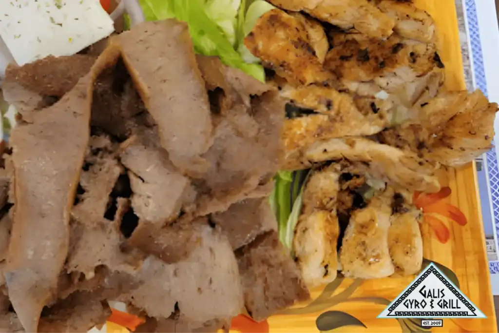 Plate of gyro meat and grilled chicken served with fresh vegetables.